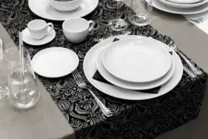 Eingedeckter Tisch mit weißem Porzellan und Besteck auf schwarzer Tischdecke